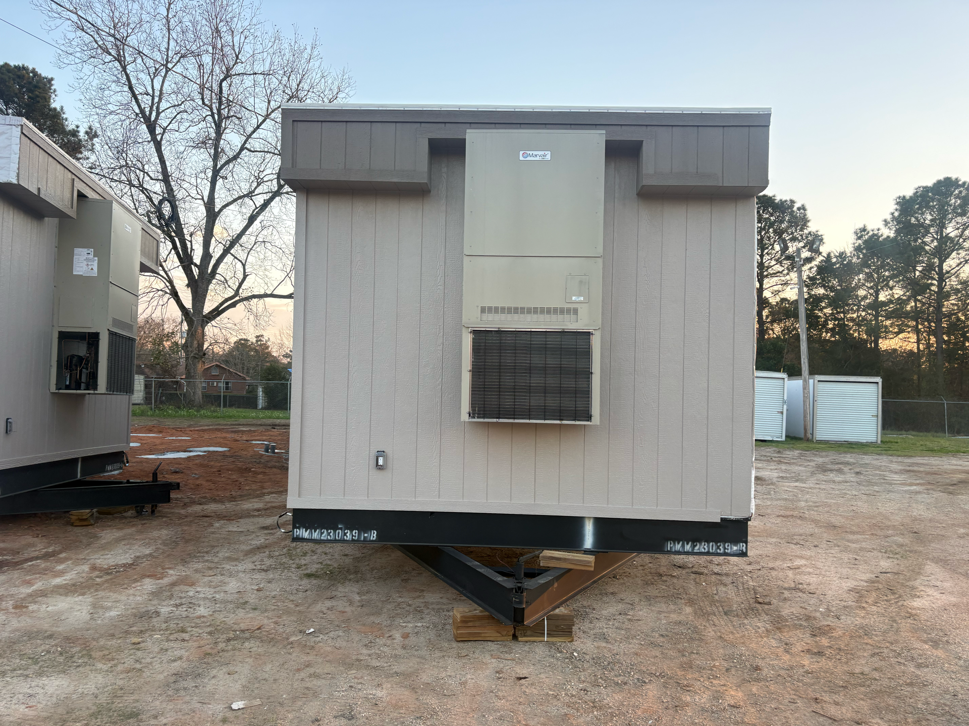Two light-colored mobile office units sit on a dirt lot, each featuring a large wall-mounted HVAC unit on the exterior.