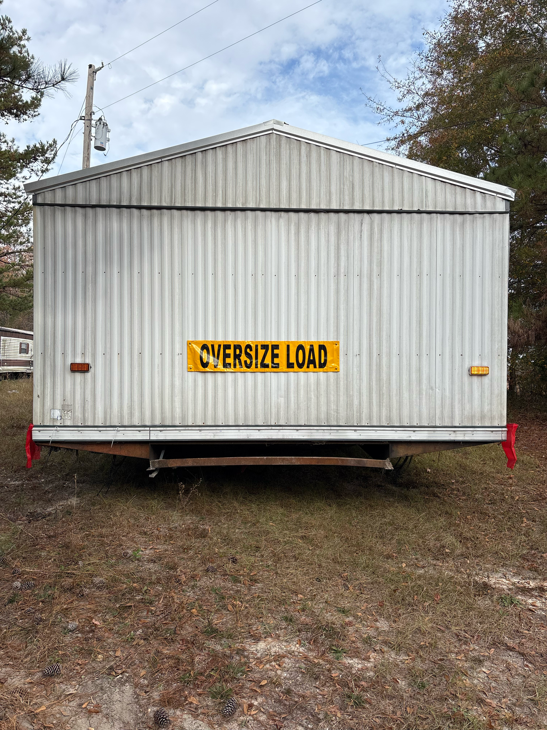 A light-colored, metal-sided portable building on a trailer frame, marked with a yellow