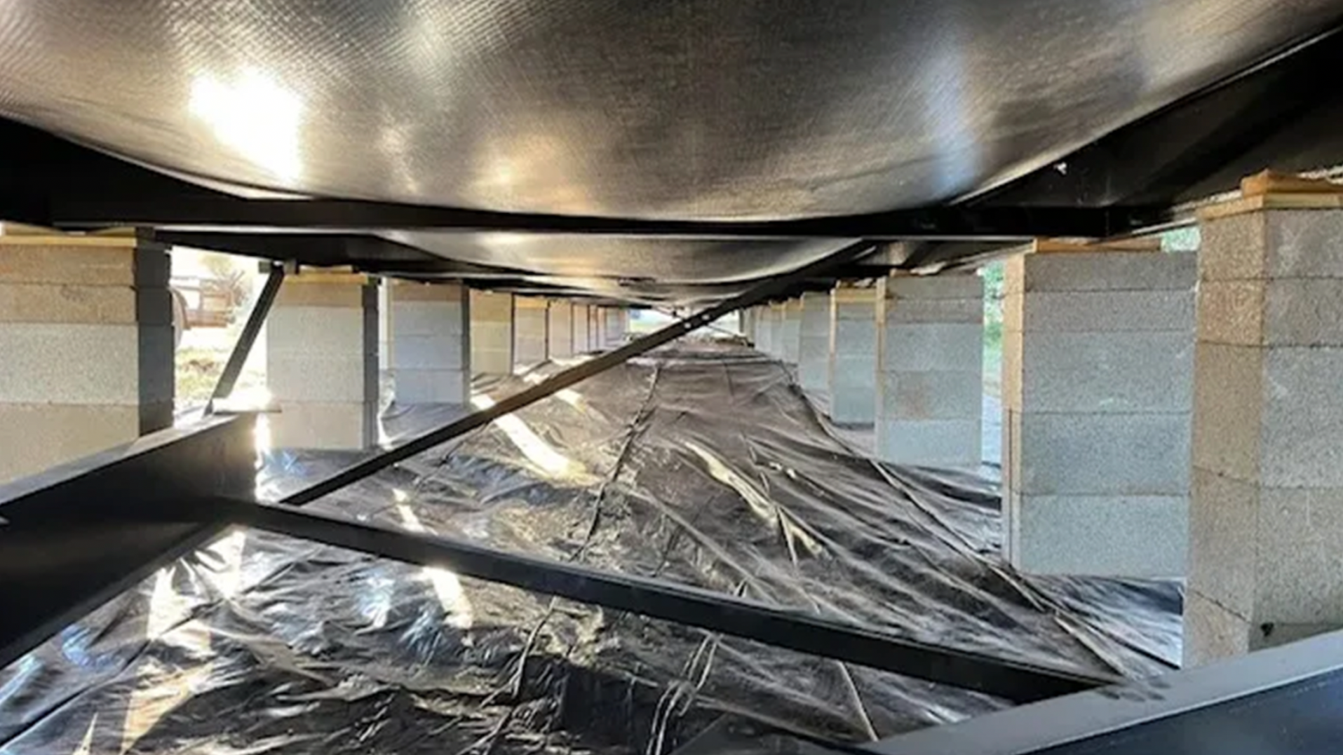 Plastic-covered crawlspace with ductwork and support pillars under a mobile home floor