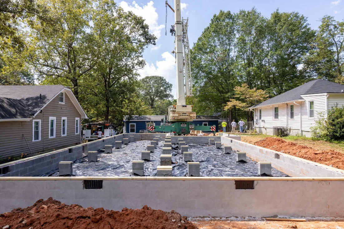 Construction workers using a crane to position a modular building section on adjustable foundation