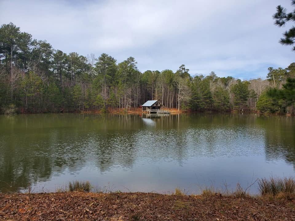 Small lake with calm water, wooded shoreline, and a lone dock with a covered shelter at center