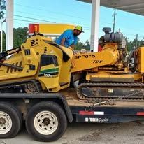 Man near yellow construction equipment on trailer at a gas station.
