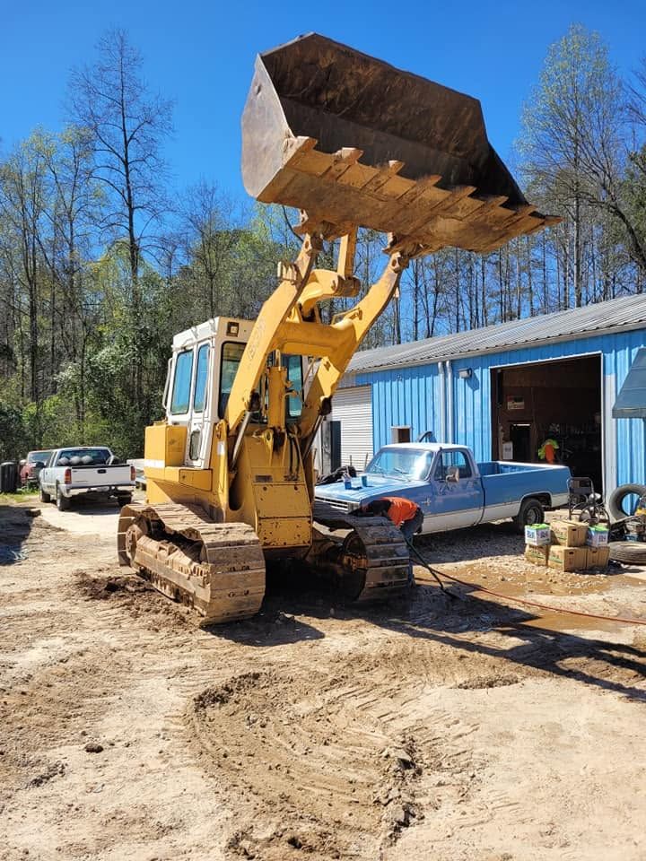 Yellow front loader with raised bucket parked beside a blue building on a muddy worksite.