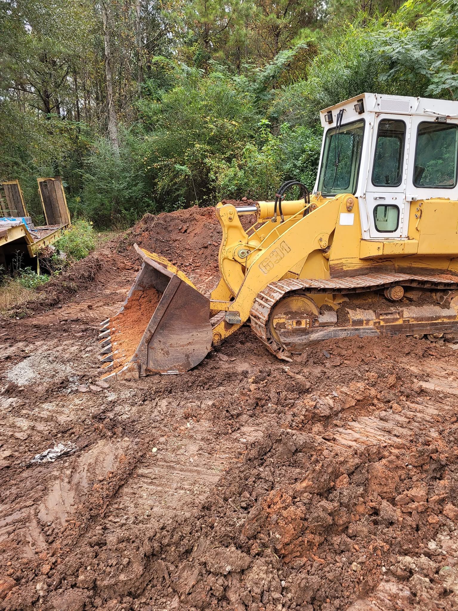 Yellow bulldozer pushing dirt on a muddy site with trees in the background