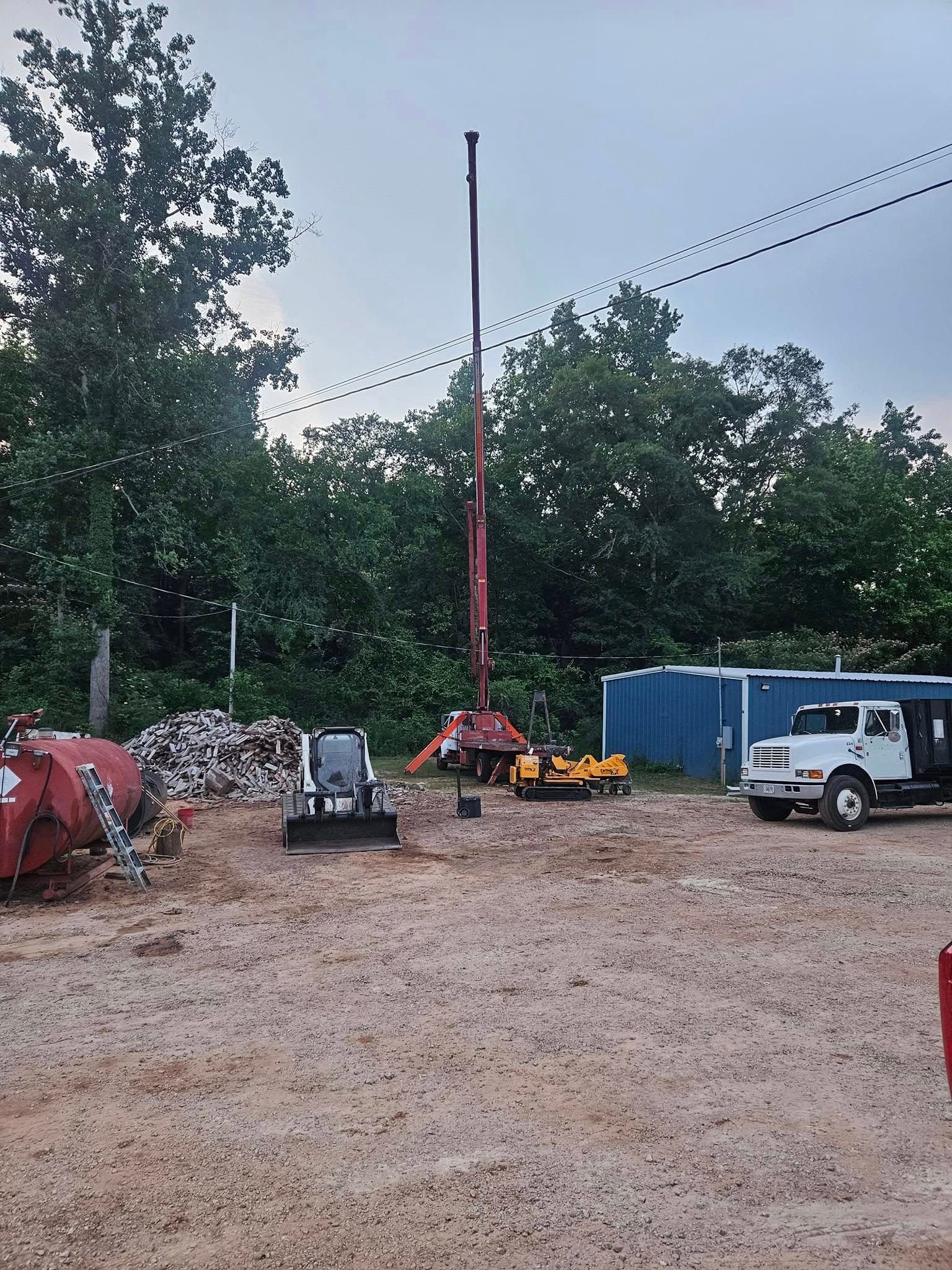 Construction site with a red crane lifting equipment beside trucks, a van, and blue containers on gravel.