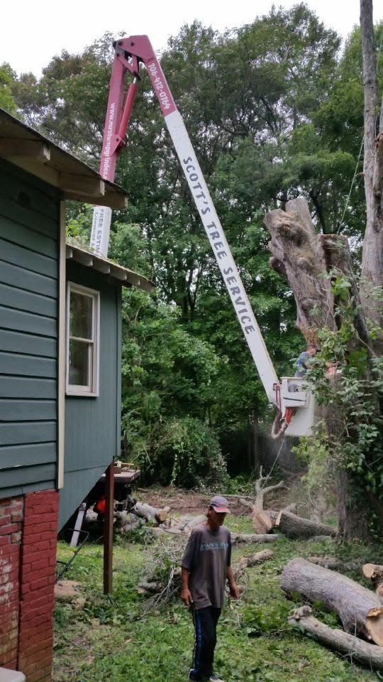 Utility bucket truck lifting a worker near a house, with a fallen tree in the yard.