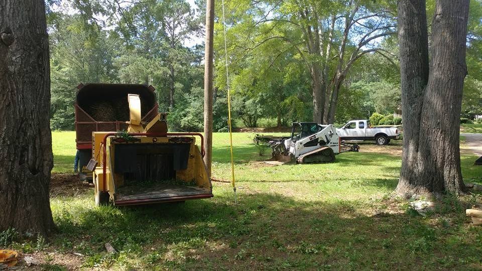 Old yellow bulldozer in a grassy yard with trees and a parked work truck in the background