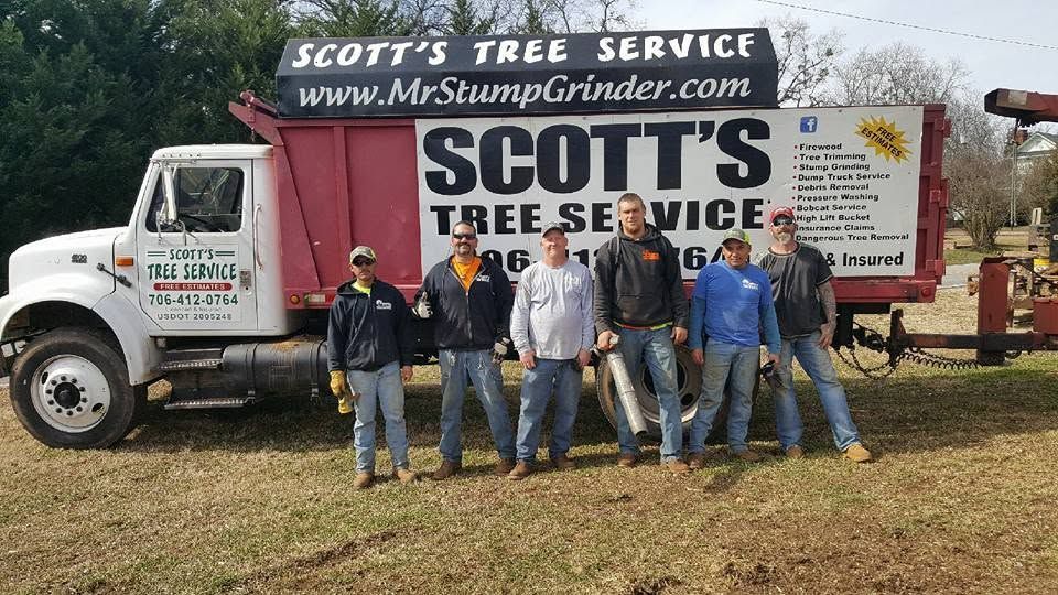 Scott’s Tree Service crew posing in front of a white truck and trailer at a grassy worksite.