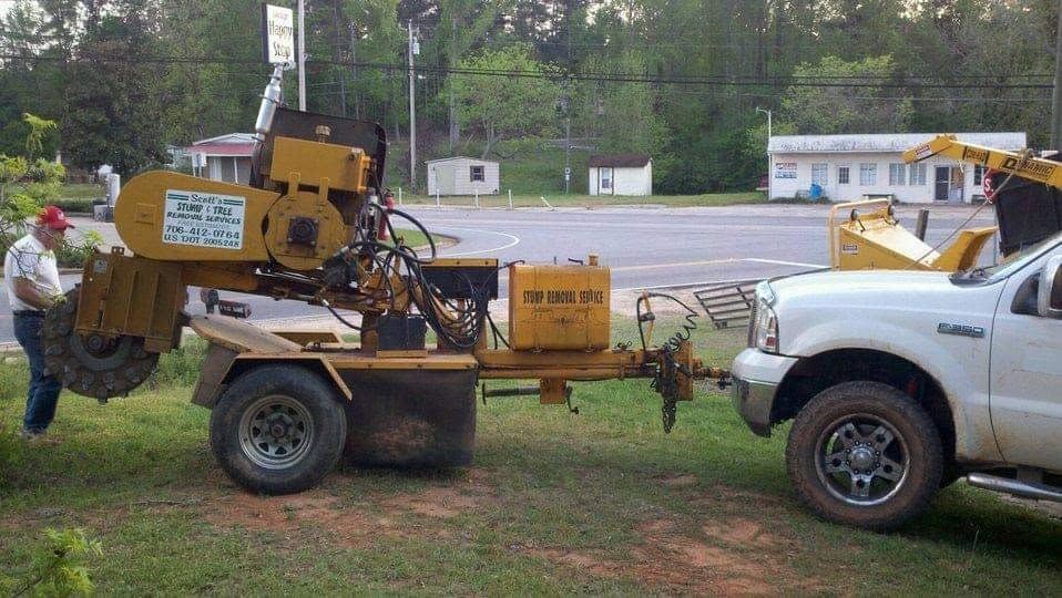 White truck towing a yellow wood chipper on a trailer in a grassy yard near a road