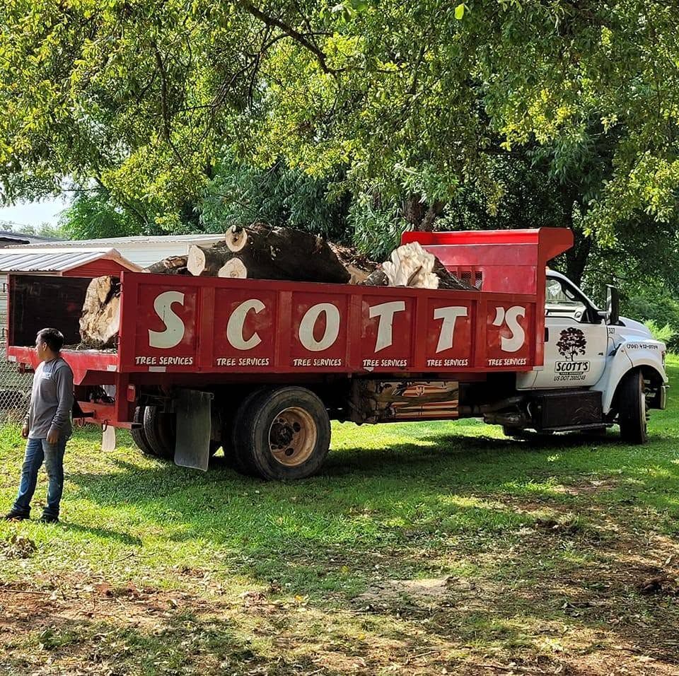 Red Scotts truck parked under a tree on grass, with a man standing nearby.