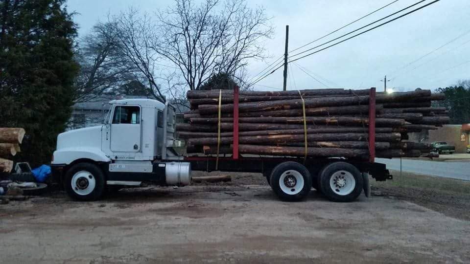 White flatbed truck loaded with long logs parked outdoors at dusk