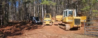 Yellow bulldozers and an excavator on a muddy forest road clearing land