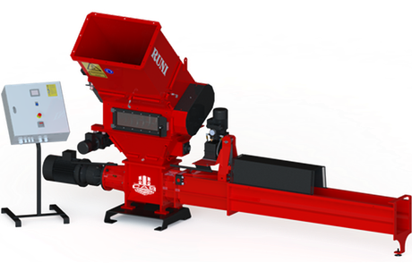 A red industrial plastic shredder with a hopper and a long horizontal discharge conveyor, accompanied by a control panel.