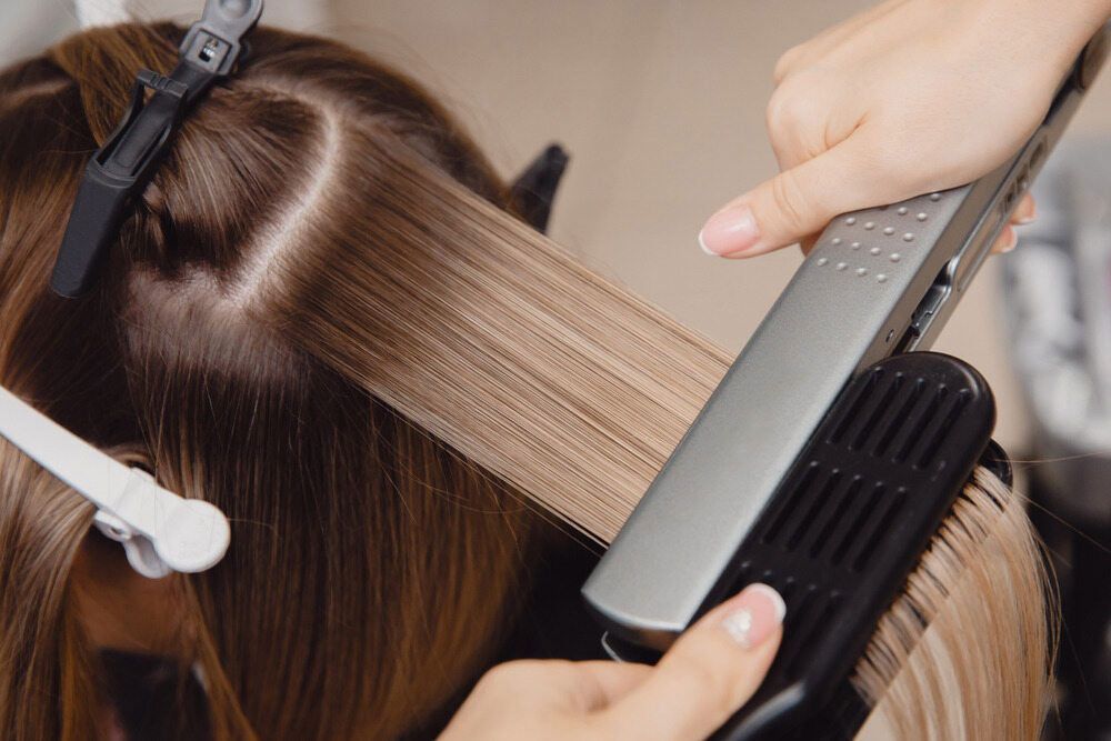 A Woman Is Getting Her Hair Straightened By A Hairdresser — Elements Hair Artists In Belmont, NSW