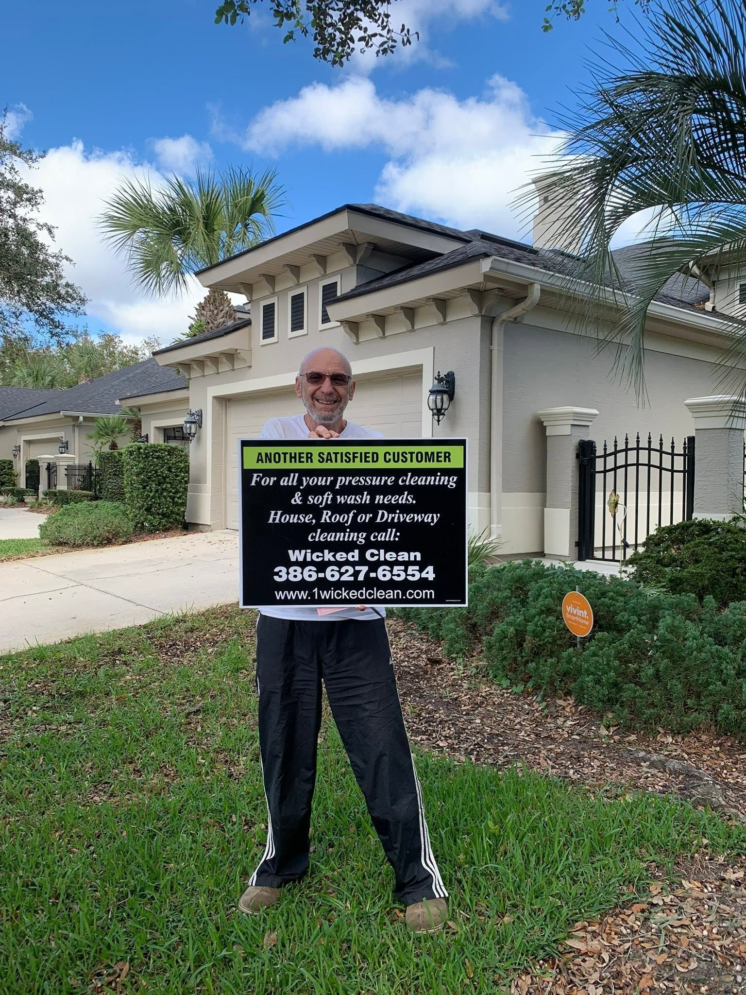 Person holding a sign outside a suburban house on a sunny day