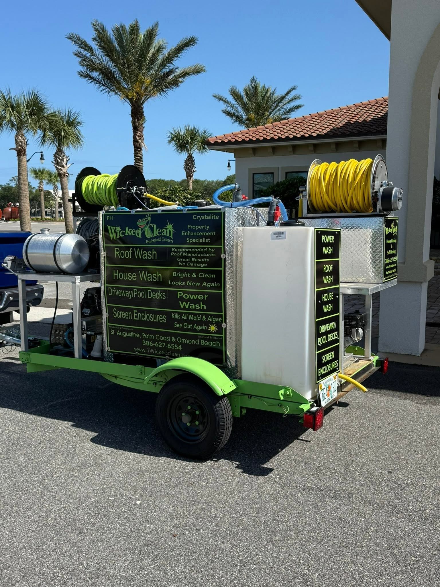 Green smoothie cart with menu boards parked outdoors beside a building and palm trees.
