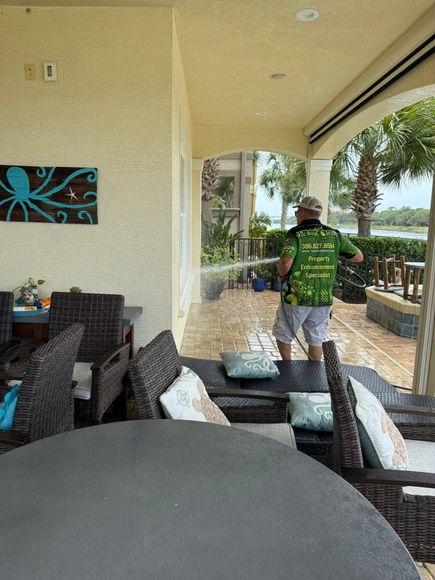 Covered patio with wicker chairs and a person in a green shirt walking outside near the water.