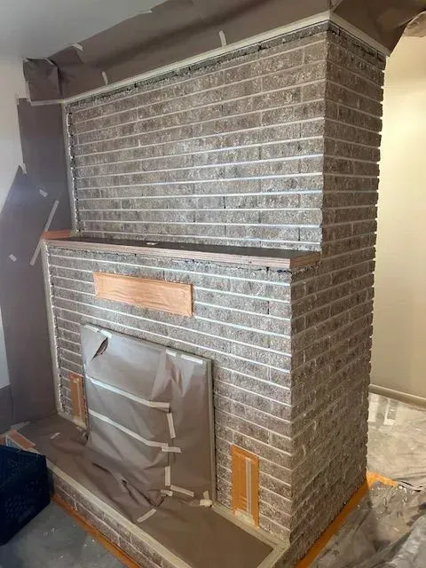 A brick fireplace and wall prepped with masking paper and tape for a painting project.