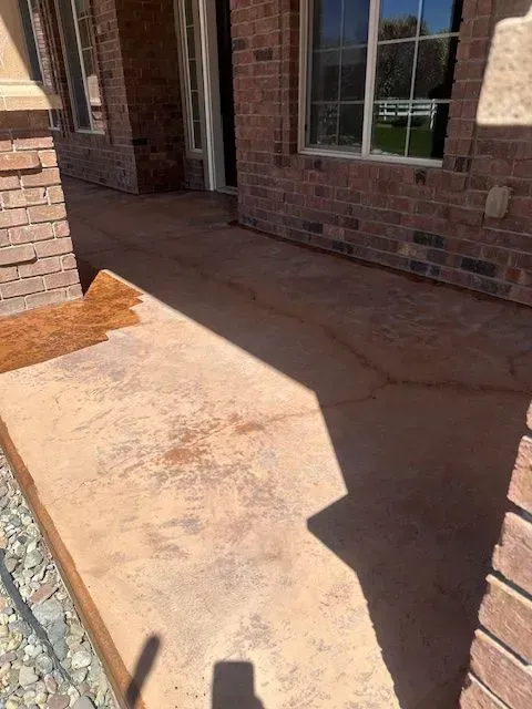 A stamped, tan-colored concrete walkway leading to a brick house entrance with large windows and a rock border.