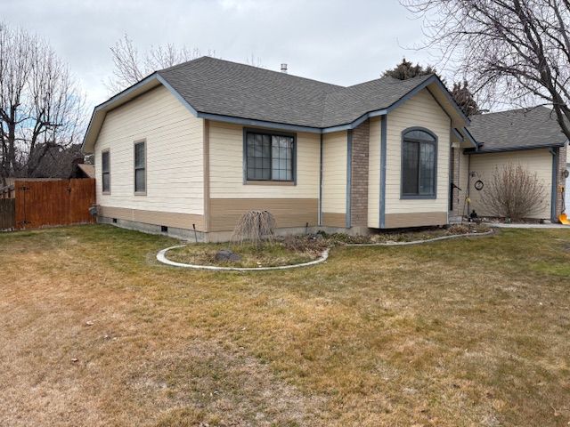 Single-story house with light beige siding, grey trim, and a roof, featuring a small landscaped garden in the front yard.