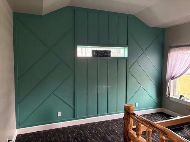 A teal accent wall with geometric wood paneling and a small rectangular window, next to a log-style stair railing.