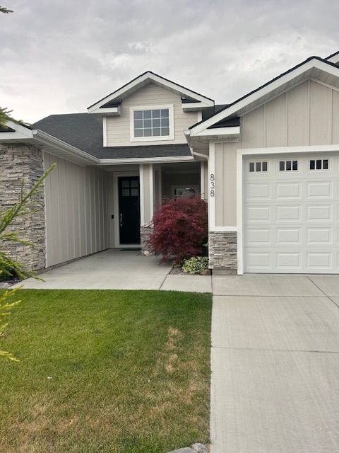 A beige house with stone accents, a dark front door, a white garage door, and a small red tree in the front entryway.