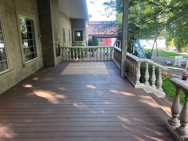 A brown wooden deck with a central light wood inlay, bordered by concrete balustrades, extending to a backyard lawn.