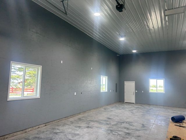 An interior view of a wide room with gray walls, a polished concrete floor, two windows, and a white door.