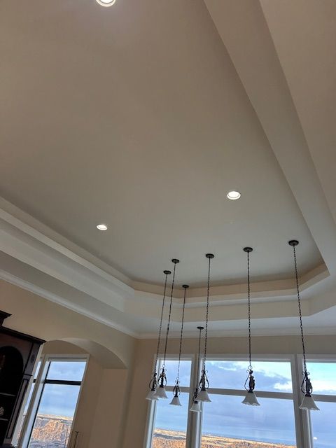 A dining area with a tray ceiling, recessed lighting, and five pendant lights hanging above a large window.