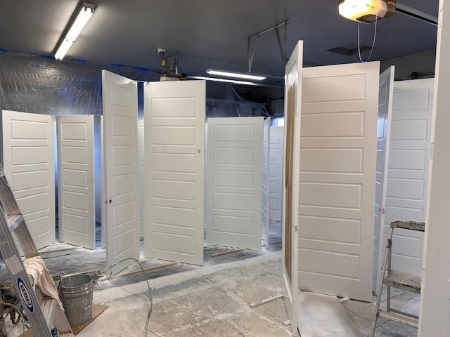 Several white, paneled interior doors standing upright in a workshop for painting.
