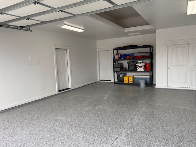Empty, well-lit garage with white walls, gray epoxy flooring, a metal storage rack, and two closed white doors.