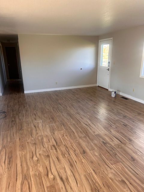 An empty room with light wood-look flooring, light-colored walls, and a single white door leading outdoors.