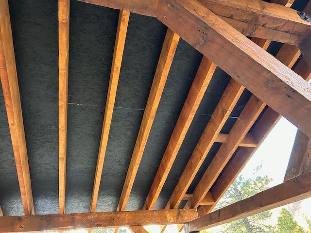 Looking up at the wooden support beams and dark panels of an open roof structure.