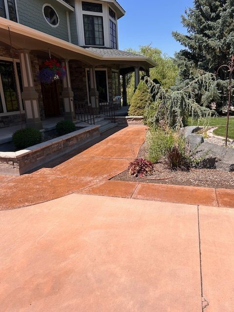 A house exterior features a terracotta-colored concrete walkway leading toward a stone-accented porch under a sunny sky.