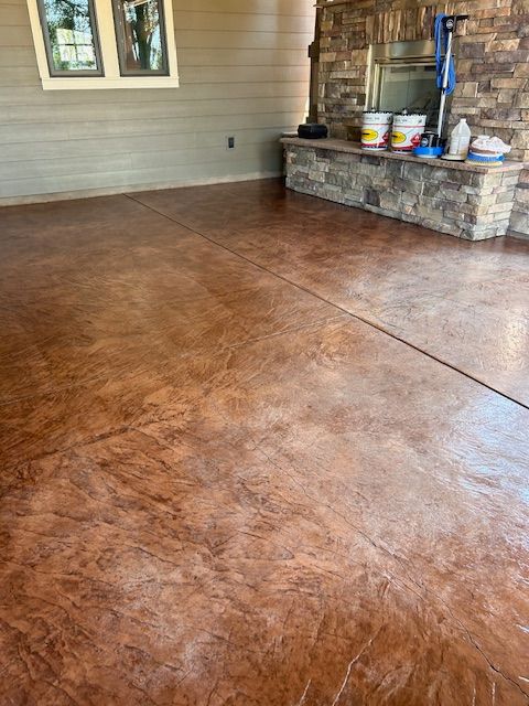 Stamped concrete patio with brown variegated texture, adjacent to a stone-faced fireplace hearth and house wall.