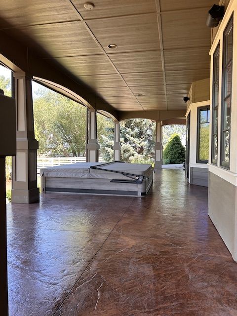 A covered patio with stamped concrete flooring, featuring a hot tub with its gray cover on under the roofed walkway.