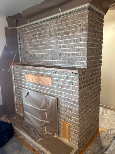 A brick fireplace surround prepared for painting, covered with masking paper and tape.