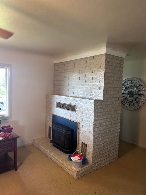 A beige brick fireplace with a wood-burning insert stands in the corner of a room, with a decorative clock on the wall.