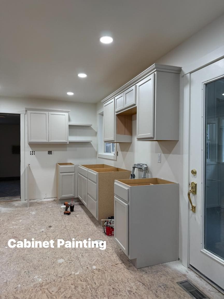 Kitchen cabinets in various stages of installation and painting, showing progress of a renovation.