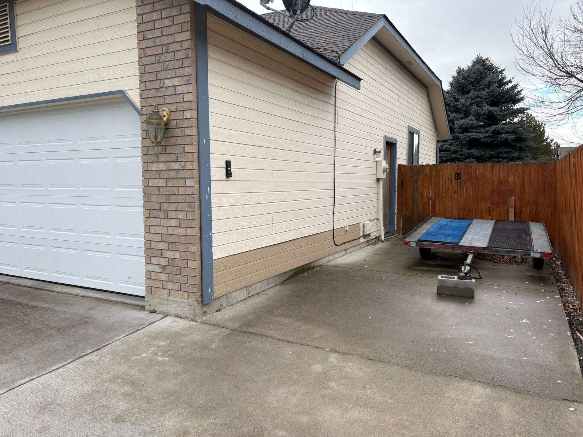Garage exterior with tan siding, brick chimney, concrete driveway, and wooden fence.
