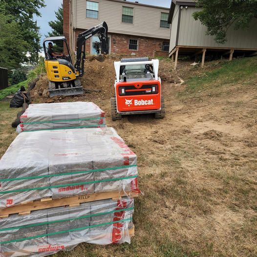 A bobcat is moving a stack of bricks on a dirt hill — Bridgeville, PA — MC Landscaping