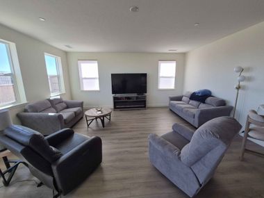 Bright living room with gray sofas, black chair, TV, coffee table, and floor lamp on wood flooring.