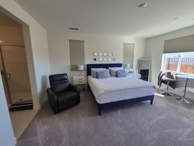 Bedroom with a bed, black recliner, mirrored dresser, and large windows with blinds