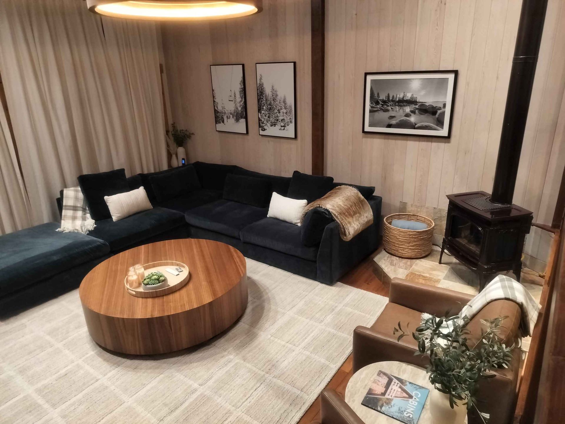 Cozy living room with black sectional sofa, round wood coffee table, wall art, and a wood stove by the window