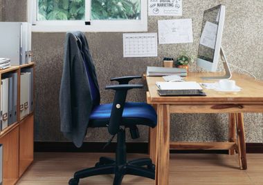 Home office desk with blue chair, jacket draped over it, and papers pinned by a window