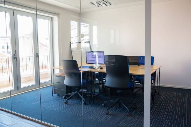 Modern office with desks, computers, and black chairs in a glass-walled meeting room