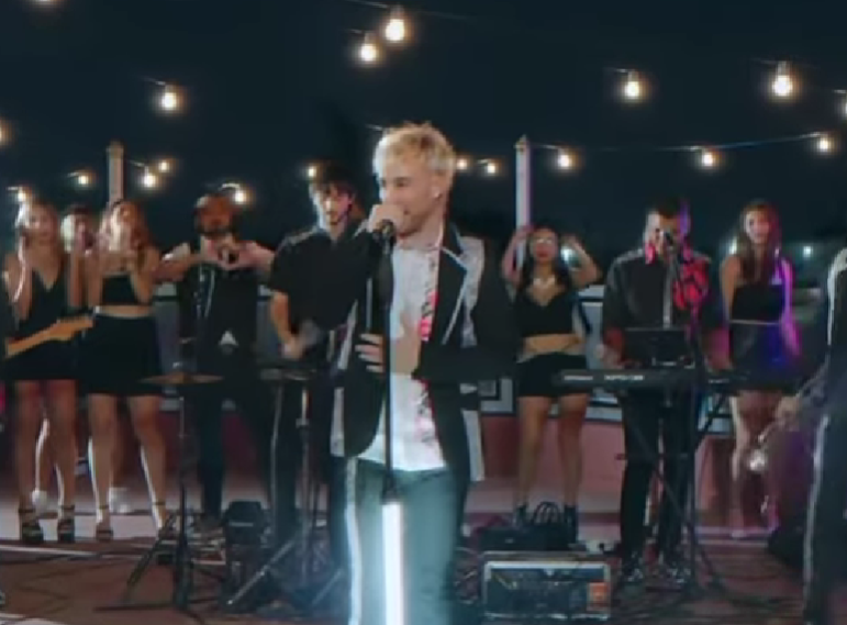 Cantante actuando en el escenario con una banda y coristas bajo luces de guirnalda.