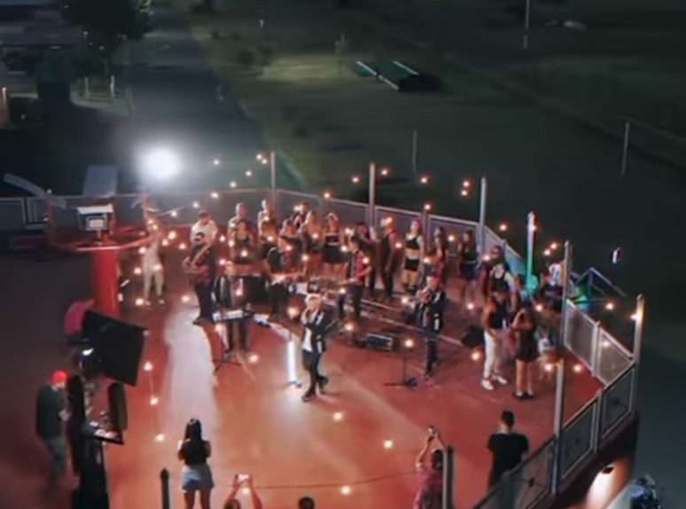 Orquesta al aire libre actuando en un escenario rojo iluminado por la noche.