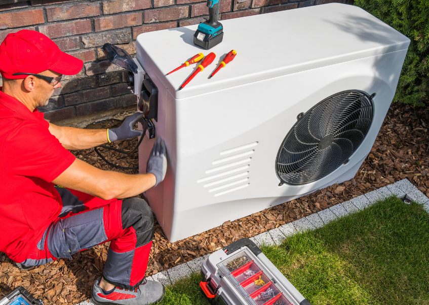 A man is working on a heat pump in a backyard.