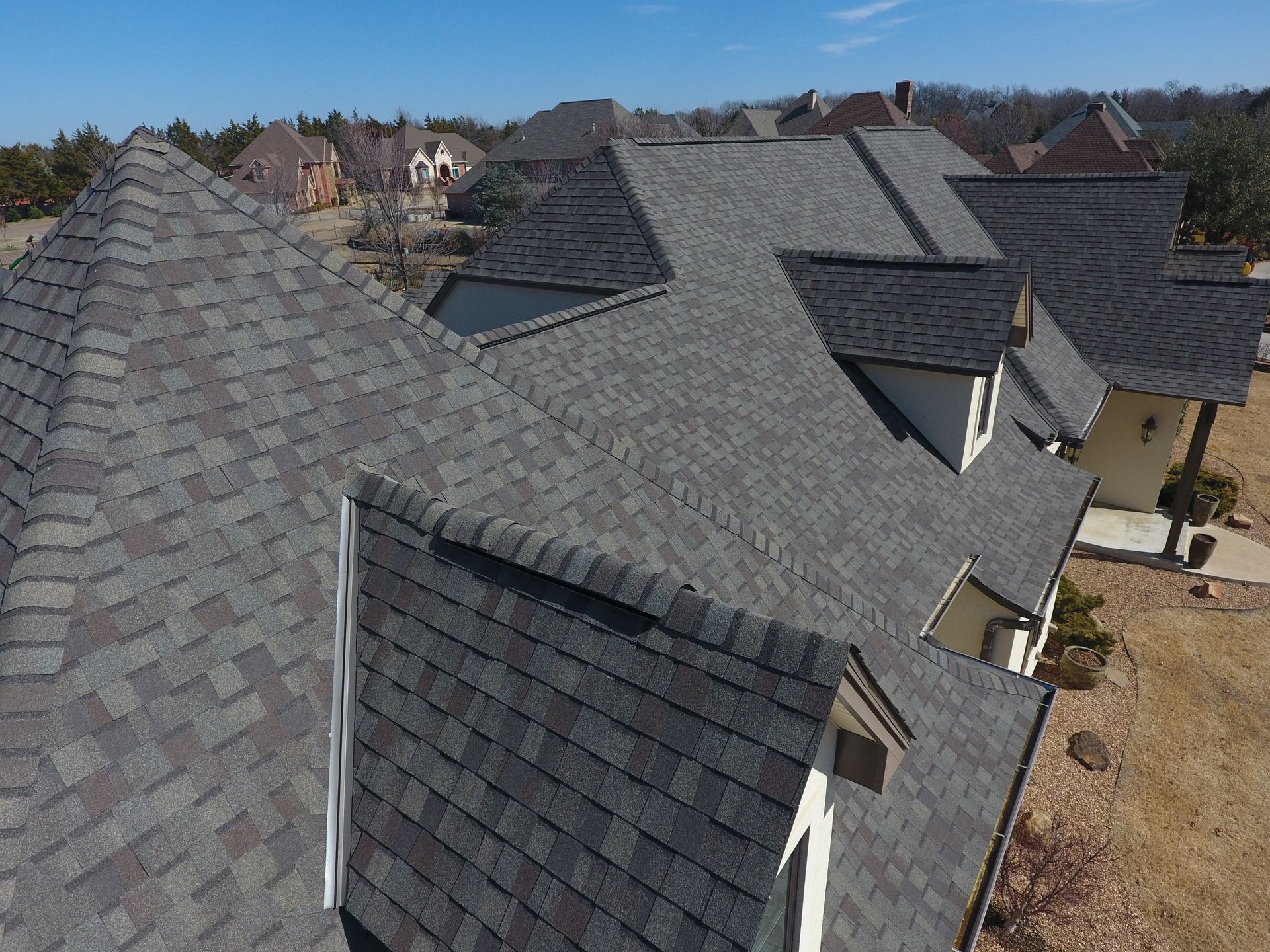 Row of dark gray shingled house roofs in a suburban neighborhood under a clear sky